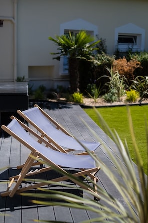 A deck with two wooden lounge chairs and a grill.