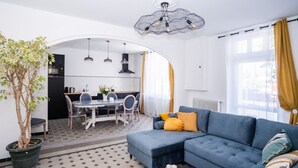 A modern living room with a blue sofa, a dining table, and a kitchen in the background.