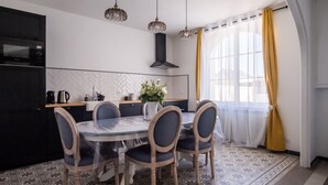 A modern kitchen with a dining area, featuring a round table with chairs, a black stove, and a large window with yellow curtains.