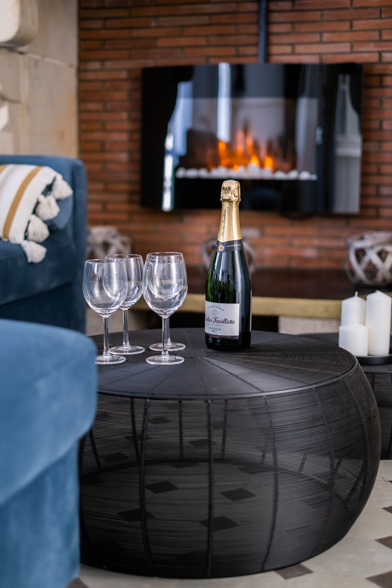 A round black table with a bottle of champagne and three glasses on it.