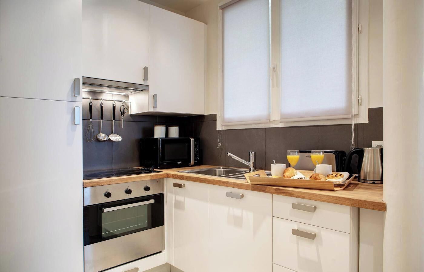 A compact kitchen with white cabinets, a black microwave, a stove, and a sink.