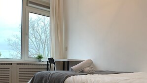 A modern bedroom with a single bed, a small table, and a window with curtains. - TU Delft Daisy room 4 (Delft)