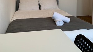 A neatly made bed with a grey and white duvet, a rolled white towel, and a black chair with a perforated backrest. - TU Delft Daisy room 4 (Delft)