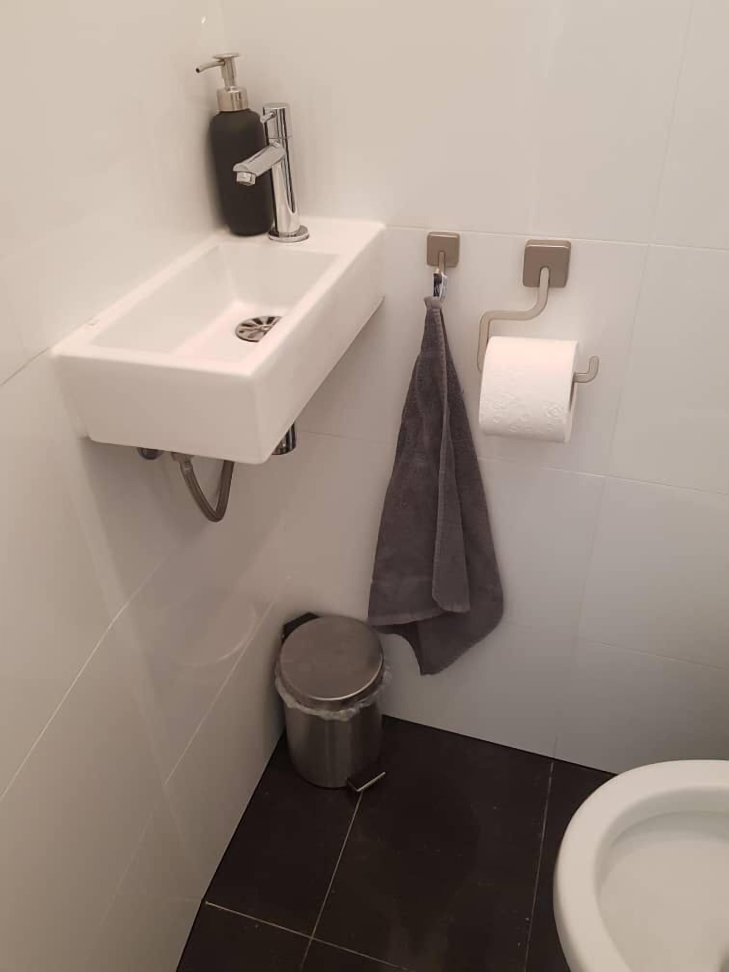 Ein Badezimmer mit einem weißen Waschbecken, einer Toilette und einem Mülleimer.