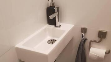 Een badkamer met een witte wastafel, een zwarte zeepdispenser, een handdoekhouder met een handdoek en een prullenbak.