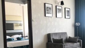 Una sala de estar moderna con un sofá gris, una cama con ropa de cama azul y tres cuadros en la pared.