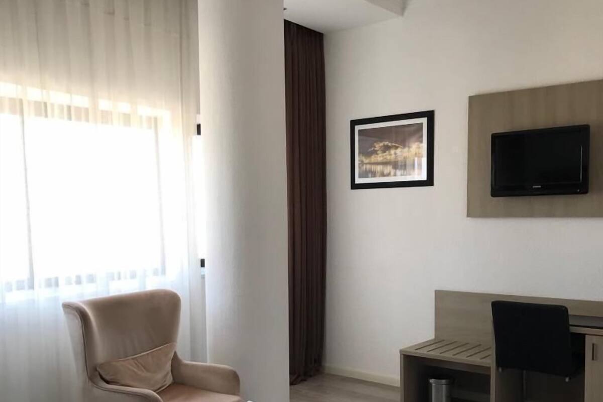 A hotel room with two beds, a desk, a chair, a TV, and a window with curtains.