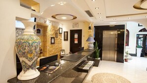 Zona de recepción con mostrador de mármol, un jarrón decorativo, mostrador de recepción, un reloj de pared y un ascensor.