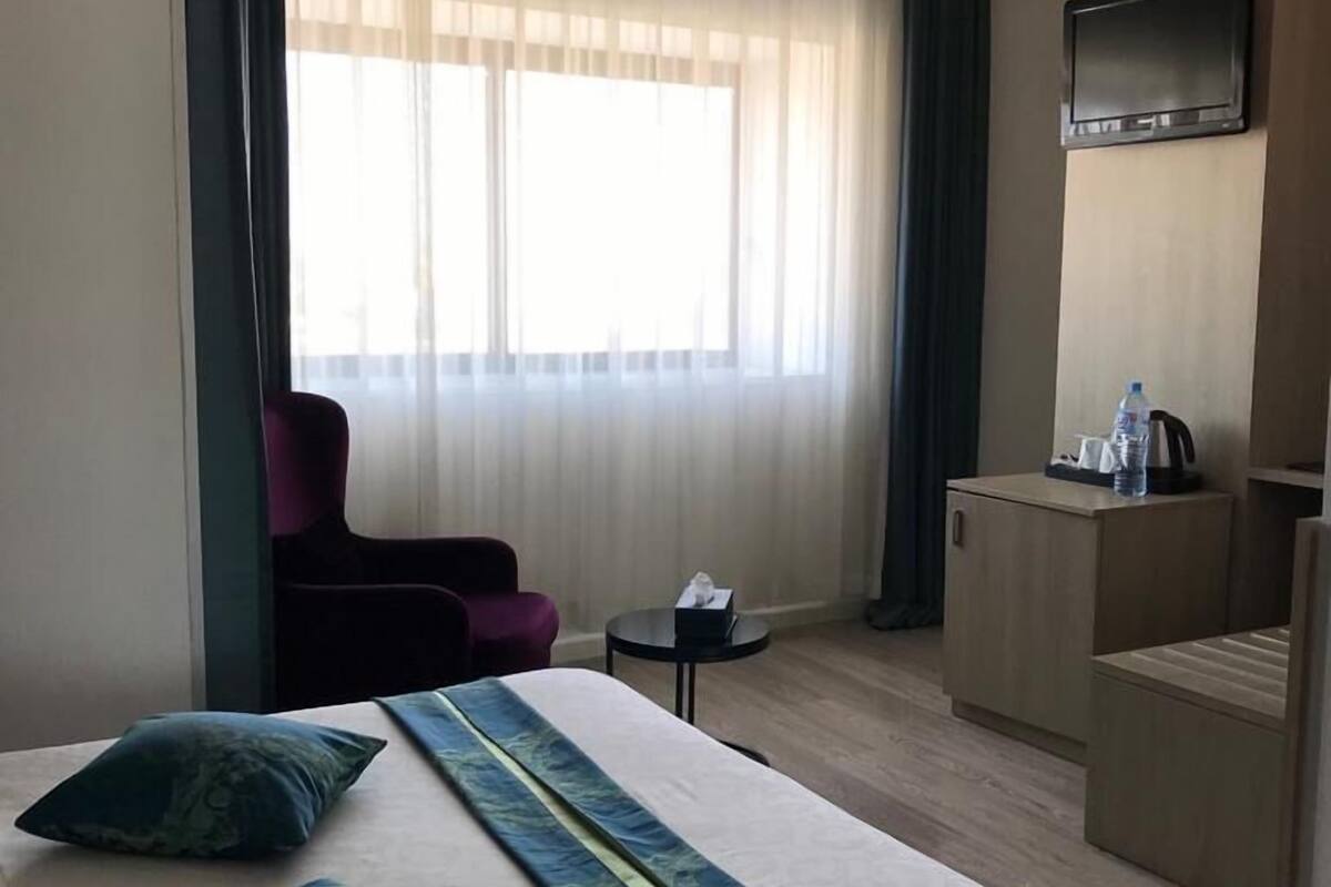 A hotel room with a large bed, a desk, a chair, a TV, and a window with curtains.