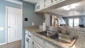 A kitchen with white cabinets, granite countertops, and stainless steel sinks. - Coastal Condo | Beach Views, Hot Tub & Gas Grills (Corpus Christi)