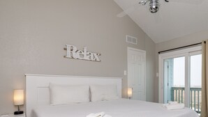 A clean, white-themed bedroom with a bed, a ceiling fan, and a view of the outdoors. - Coastal Condo | Beach Views, Hot Tub & Gas Grills (Corpus Christi)
