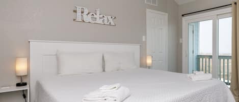 A clean, white-themed bedroom with a bed, a ceiling fan, and a view of the outdoors.