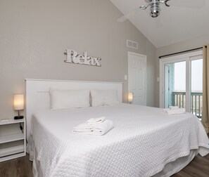 A clean, white-themed bedroom with a bed, a ceiling fan, and a view of the outdoors. - Coastal Condo | Beach Views, Hot Tub & Gas Grills (Corpus Christi)