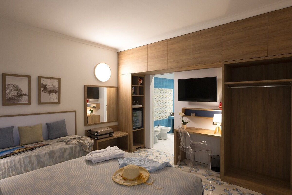 A hotel room with two beds, a desk with a chair, a TV, and a bathroom visible through an open door.