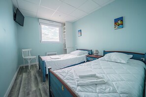Une chambre avec deux lits, une fenêtre, une télévision et une petite table.