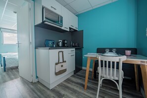 Une cuisine compacte équipée d’un four à micro-ondes, d’une machine à café et d’une petite table avec une chaise.