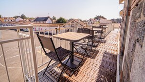 A rooftop terrace with tables and chairs, a view of surrounding buildings, and a brick wall.