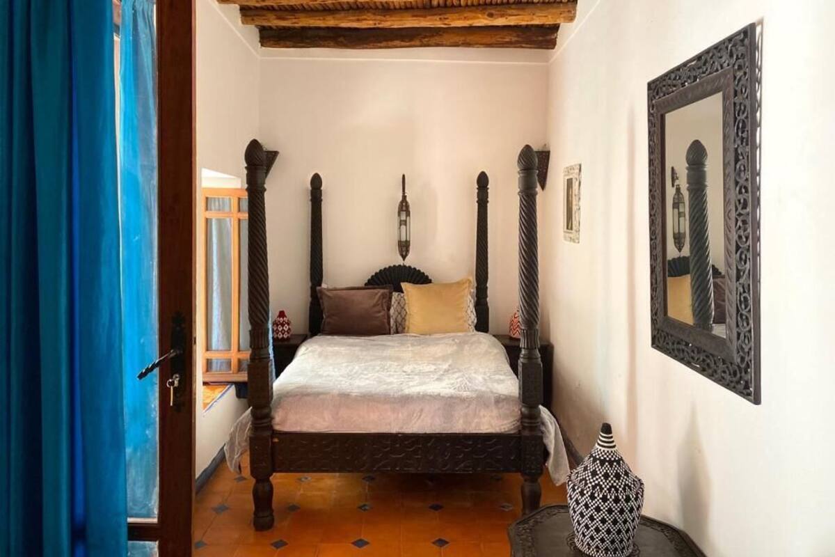 A traditional bedroom with a four-poster bed, a wooden ceiling, and a large mirror on the wall.