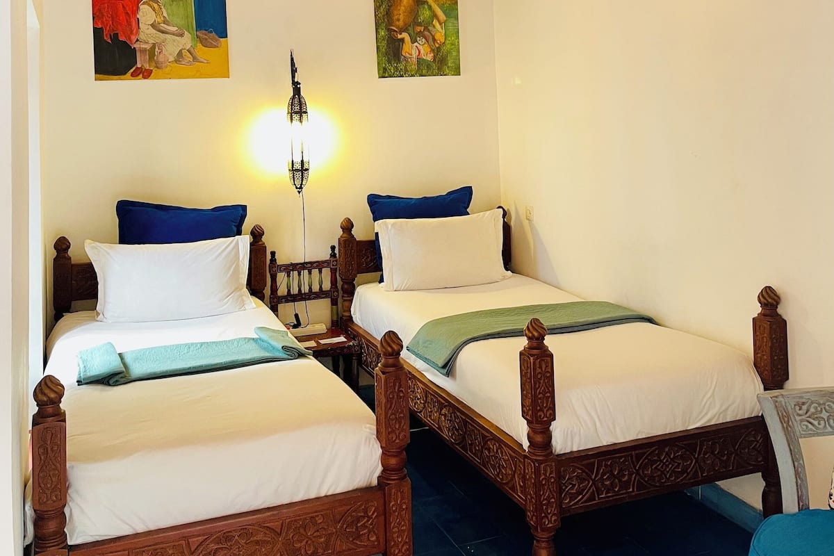 A room with two wooden beds, a hanging light fixture, and two wall-mounted paintings.