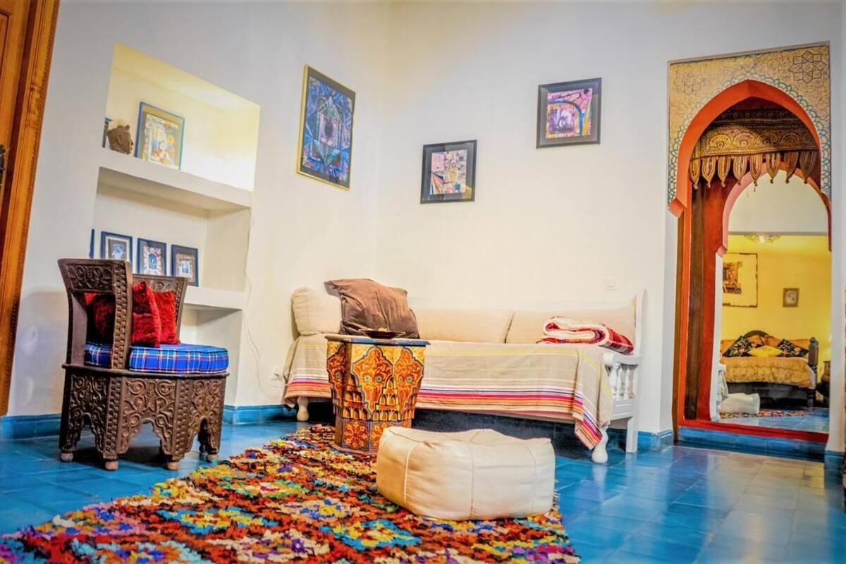 A room with a sofa, a patterned rug, a decorative chair, and a small table with a cushion.