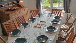 Un espace repas avec une longue table dressée pour six personnes, entourée de chaises en bois.