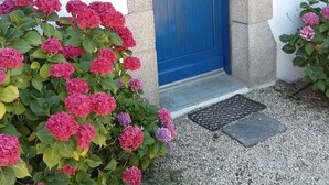 Une porte bleue avec une petite fenêtre, un mur de pierre et un chemin de gravier menant à un paillasson.