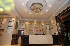 A hotel reception area with a marble counter, a chandelier, and a wall with a logo. - Fuli Business Hotel (Chengmai)