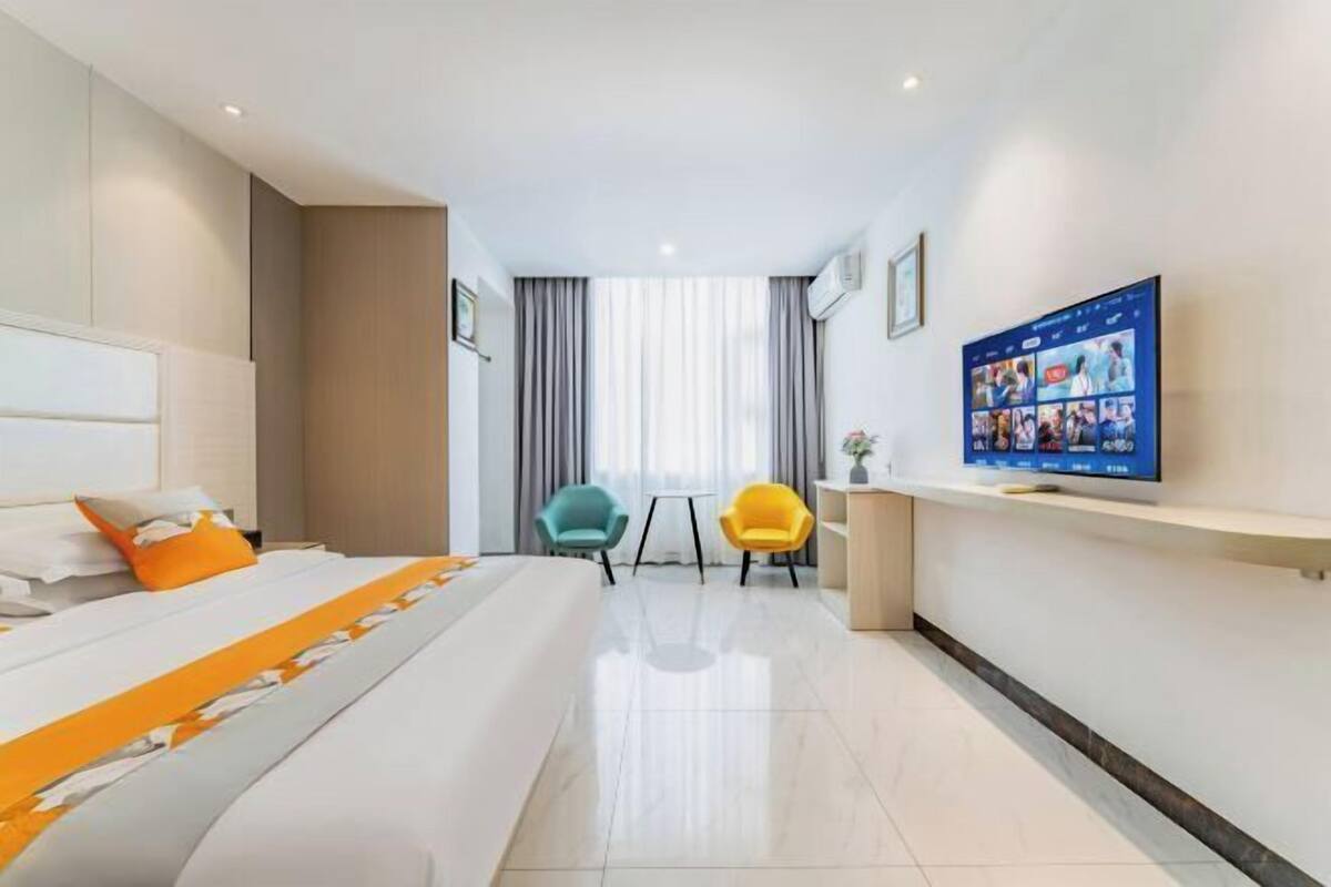 A modern hotel room with a large bed, a television, two chairs, and a small table.