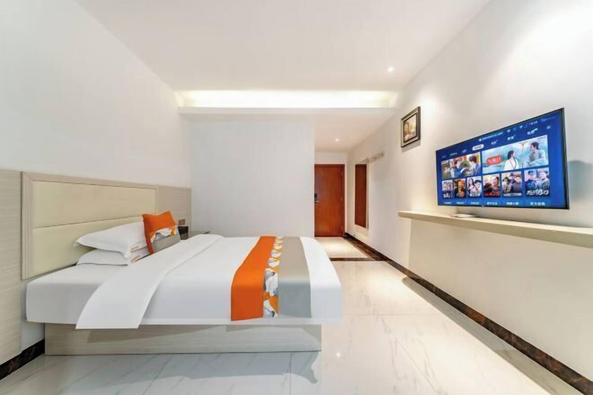 A hotel room with a bed, a television on the wall, and a hallway leading to another room.