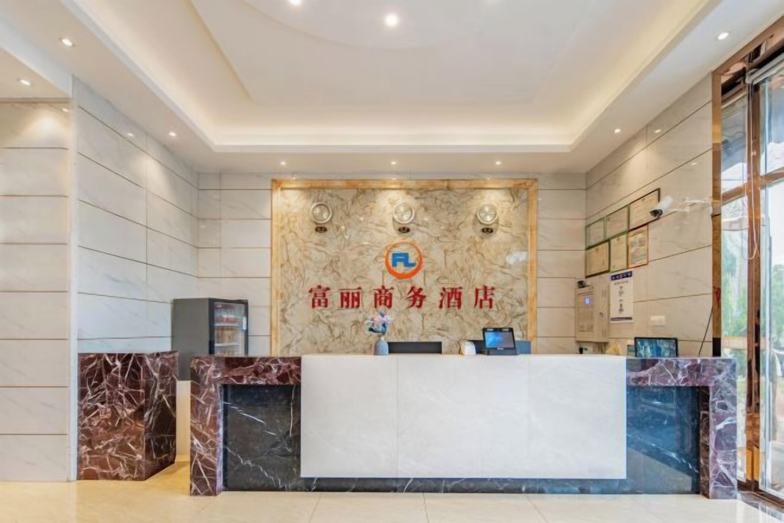 Un'area reception di un hotel con una scrivania in marmo, una bacheca informativa a parete e un'ampia finestra sulla destra.