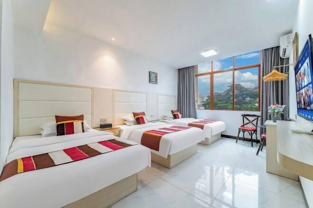 A hotel room with three beds, a desk, and a large window with a view.