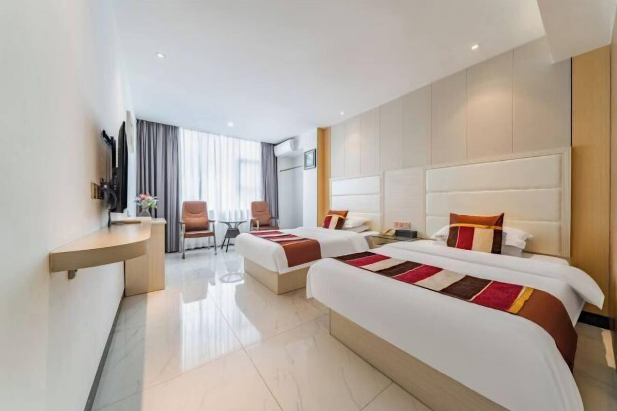 A hotel room with two beds, a desk, a chair, and a TV.