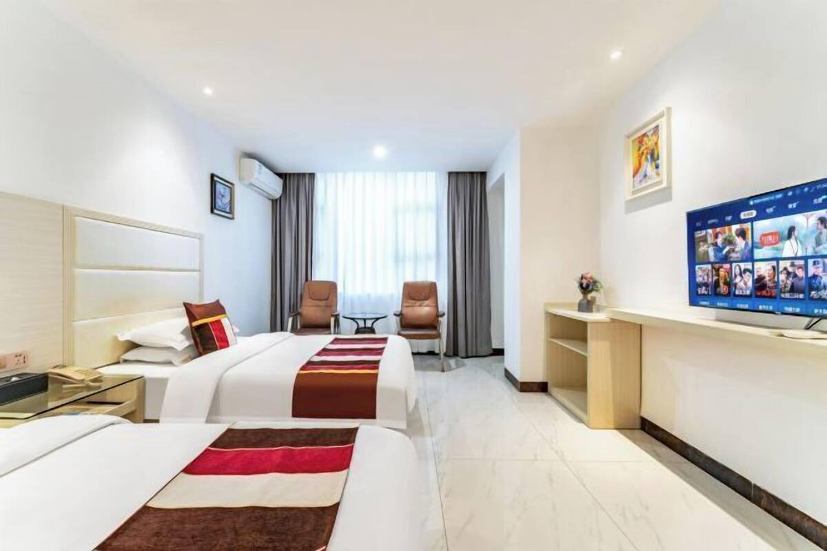 A hotel room with two beds, a TV, a desk, and a window with curtains.