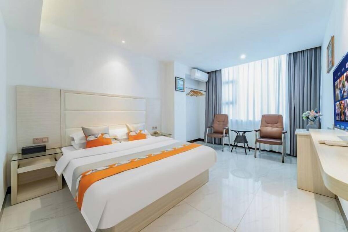 A hotel room with a large bed, a desk, two chairs, and a window with curtains.