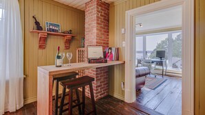 A cozy kitchen with wooden walls, a brick chimney, a bar area with stools, and a view through a glass door.