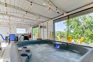 Un bain à remous à l’extérieur, avec un revêtement en pierre, entouré de meubles de jardin et doté de grandes fenêtres offrant une vue sur les arbres.