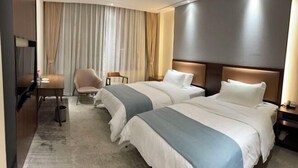 A hotel room with two beds, a desk, a chair, and a large window with curtains.