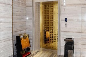 Una pared de mármol, una puerta de ascensor dorada y un cubo de basura.