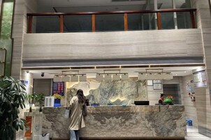 Zona de recepción de hotel con mostrador de mármol, pantalla digital y balcón en el segundo piso.