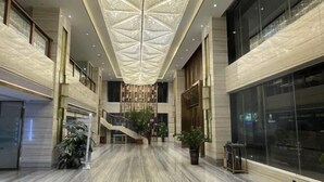 A spacious lobby with a high ceiling, marble flooring, and a central staircase.