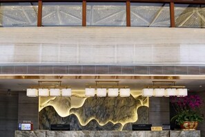 A reception desk with a marble back wall, a ceiling with a geometric pattern, and a potted plant. - Yanfu Hotel (Lianjiang)