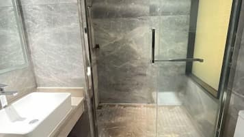 Un bagno moderno con cabina doccia in vetro, lavandino bianco e parete rivestita in marmo.