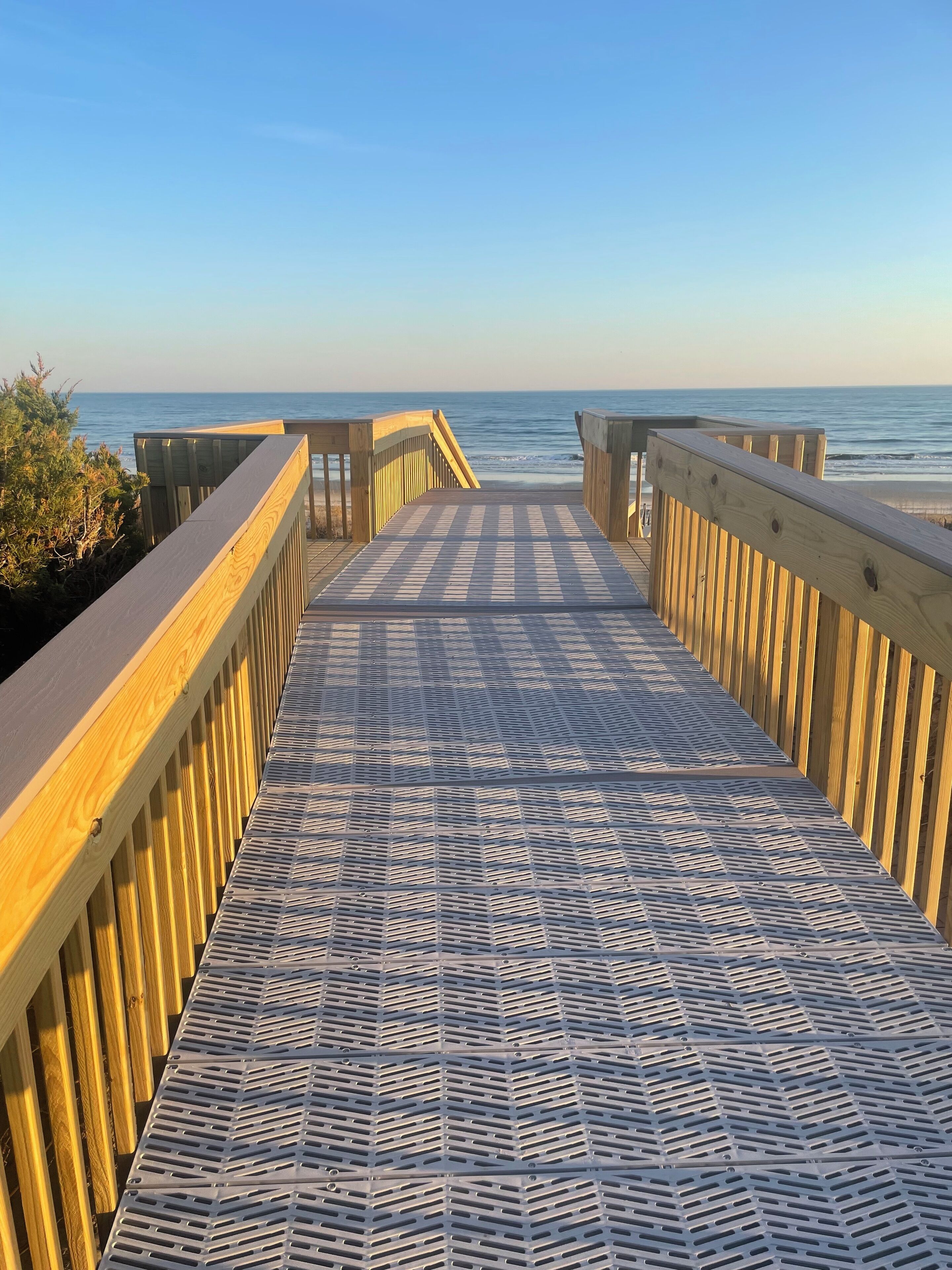 A wooden boardwalk leading to the beach with a patterned metal floor.
