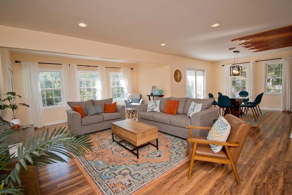 A spacious living room with a large sofa set, a coffee table, and a dining area with chairs. - Emerald Dream, Oceanside House in Emerald Isle, NC (Emerald Isle)