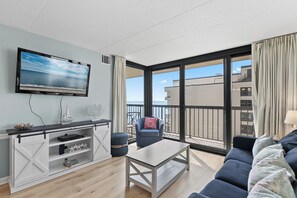 Ein modernes Wohnzimmer mit Fernseher, einer Couch, einem Couchtisch und einem Balkon mit Meerblick.