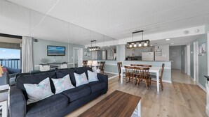 Una sala de estar moderna con un sofá oscuro, una mesa de centro de madera y un comedor con sillas de madera y una mesa blanca.