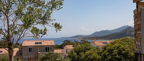 A coastal residential area with stone buildings, a view of the sea, and a mountain in the background.