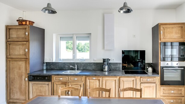Une cuisine moderne avec des meubles en bois, un grand îlot central, des appareils électroménagers en acier inoxydable et des luminaires suspendus.
