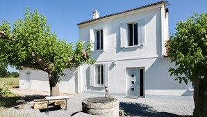 Un bâtiment blanc avec un toit en tuiles, un puits et un banc au premier plan.