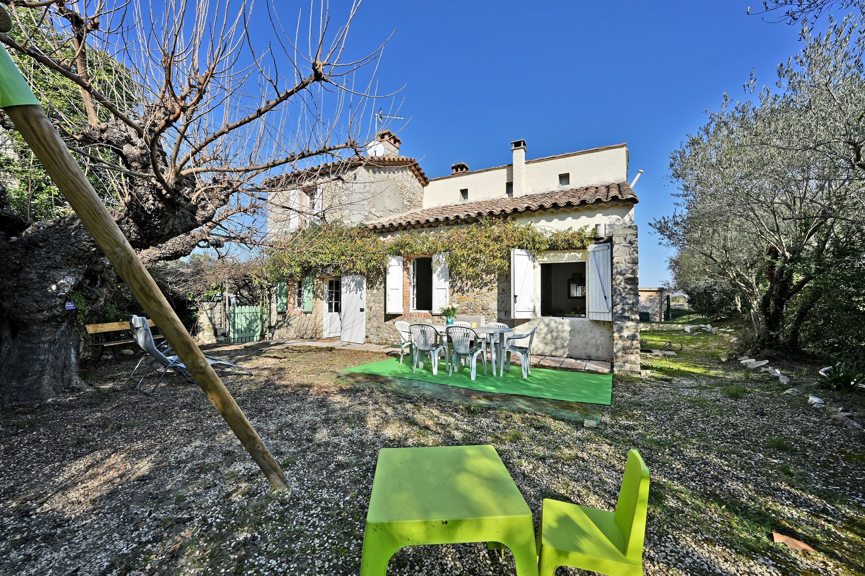 A rustic stone building with a tiled roof, a patio with outdoor furniture, and a well-maintained garden.